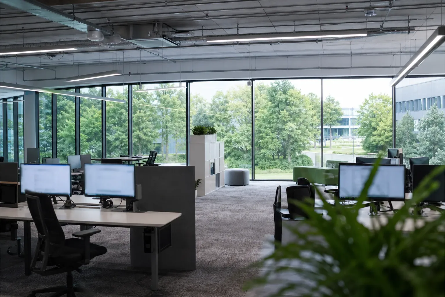 Open space d’une entreprise tertiaire avec de grandes baies vitrées donnant sur un parc d’activités arboré
